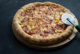Tasty hawaiian pizza( cheese ,crispy bacon and pineapple)and pizza cutter wheel.Dark background with Copy space .