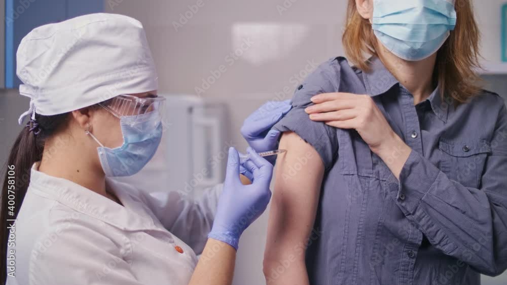 Medical Nurse in Safety Gloves and Protective Mask is Making a Vaccine Injection to a Patient. Doctor Uses Hypodermic Needle and a Syringe to Put a Shot of Drug as Treatment. Vaccination Medical Nurse in Safety Gloves and Protective Mask is Making a Vaccine Injection to a Patient. Doctor Uses Hypodermic Needle and a Syringe to Put a Shot of Drug as Treatment. Vaccination