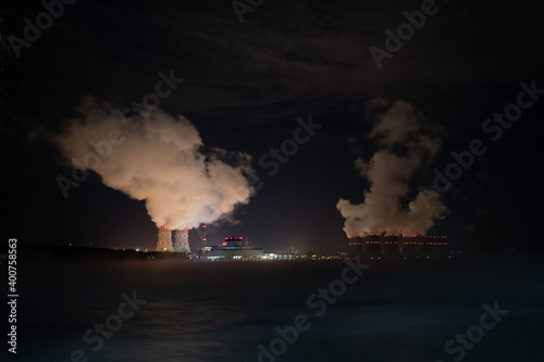 The steam pipes cooling towers of a nuclear power plant emit steam at night. Operation of a nuclear power plant at night. Energy. Nuclear fuel. Provision of electricity and heat