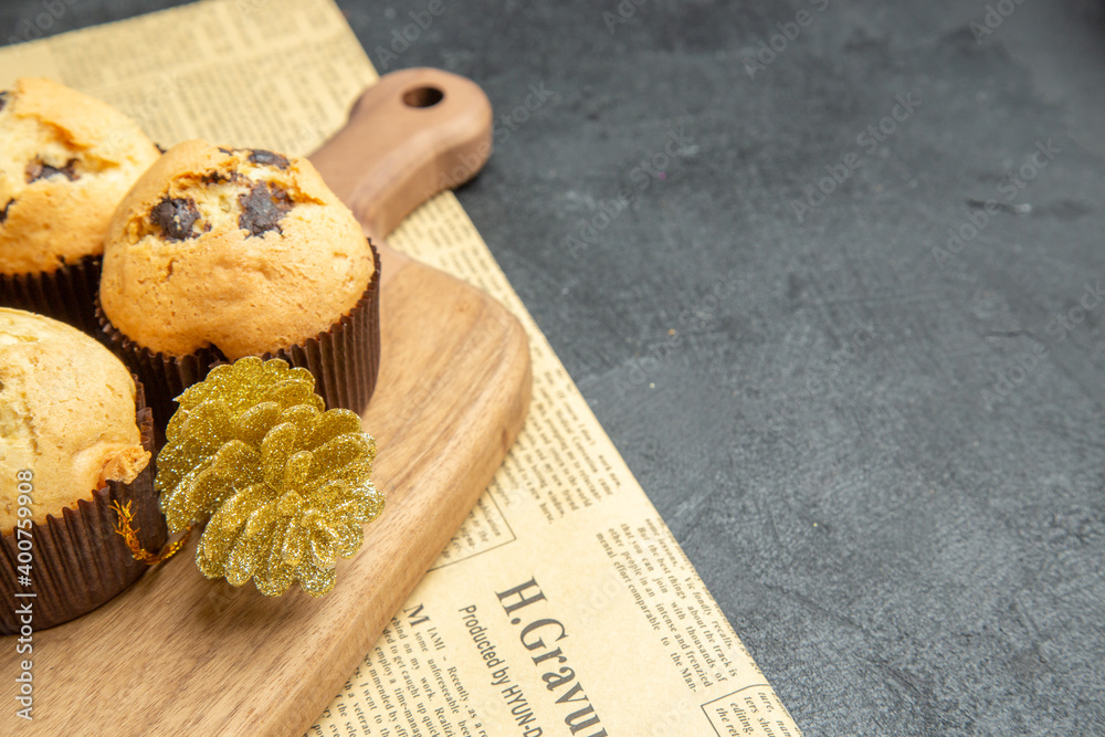 Half shot of freshly baked small cupcakes with accessories on wooden cutting board on newspaper on dark background