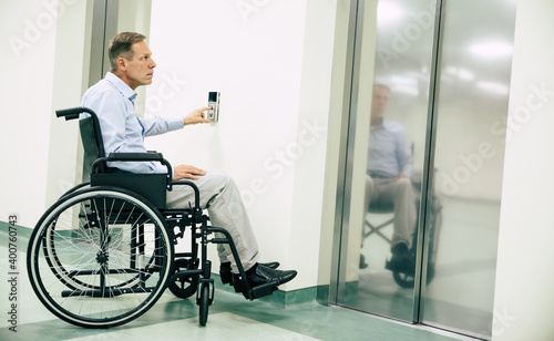 Ill senior man in a wheelchair is pushing on the button for call elevator in the hospital photo