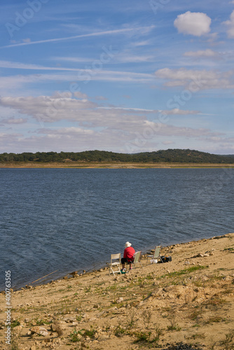 Caucasian senior woman sitting on a chair with a straw hat on a dam lake reservoir in Alentejo, Portugal