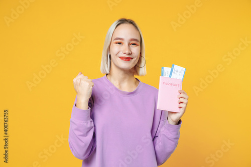 Traveler tourist woman in purple basic shirt hold passport ticket doing winner gesture isolated on yellow orange background. Passenger traveling abroad on weekends getaway. Air flight journey concept.