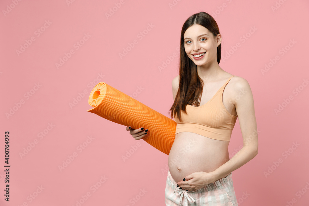 Young strong sporty fitness pregnant woman keeping hands on big belly stomach tummy with baby hold yoga mat isolated on pastel pink background studio. Maternity family pregnancy expectation concept Young strong sporty fitness pregnant woman keeping hands on big belly stomach tummy with baby hold yoga mat isolated on pastel pink background studio. Maternity family pregnancy expectation concept