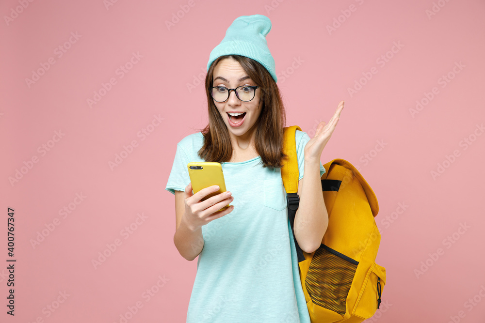 Surprised young woman student in t-shirt hat glasses backpack spreading hands using mobile cell phone typing message isolated on pink background. Education in high school university college concept. Surprised young woman student in t-shirt hat glasses backpack spreading hands using mobile cell phone typing message isolated on pink background. Education in high school university college concept.
