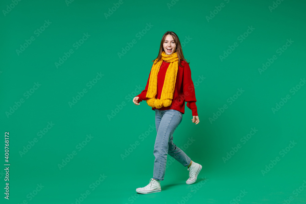Full length side view of excited cheerful young brunette woman 20s in casual knitted red sweater yellow scarf walking going looking camera isolated on bright green color background studio portrait. Full length side view of excited cheerful young brunette woman 20s in casual knitted red sweater yellow scarf walking going looking camera isolated on bright green color background studio portrait.