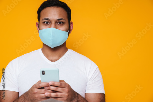 Asian man in face mask using mobile phone and looking at camera