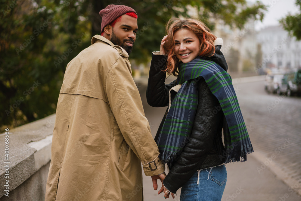 Multinational couple holding hands together and smiling while walking Multinational couple holding hands together and smiling while walking