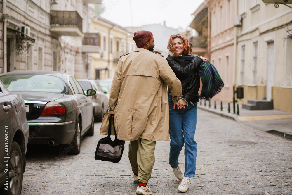 Multinational couple holding hands together and smiling while walking Multinational couple holding hands together and smiling while walking