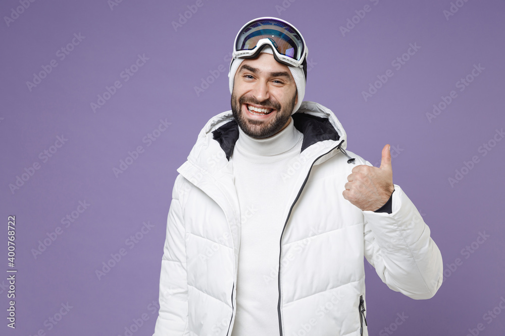 Smiling skier man in warm windbreaker jacket ski goggles mask showing thumb up going to spend extreme weekend winter season in mountains isolated on purple background. People lifestyle hobby concept. Smiling skier man in warm windbreaker jacket ski goggles mask showing thumb up going to spend extreme weekend winter season in mountains isolated on purple background. People lifestyle hobby concept.