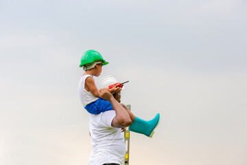 Cheerful african american father and son in hard hat, Happy dad carrying son on shoulders