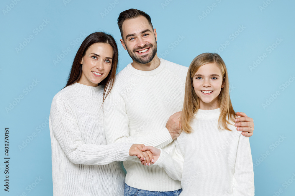 Cheerful young happy parents mom dad with child kid daughter teen girl in basic white sweaters hugging holding hands isolated on blue color background studio portrait. Family day parenthood concept. Cheerful young happy parents mom dad with child kid daughter teen girl in basic white sweaters hugging holding hands isolated on blue color background studio portrait. Family day parenthood concept.