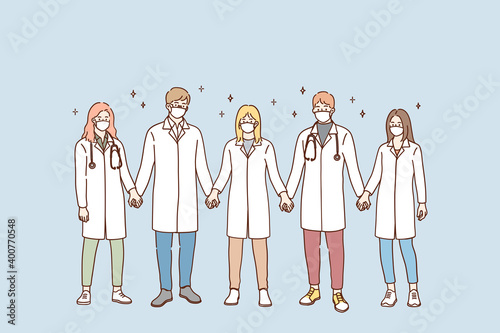 Doctors teamwork, uniting efforts against COVID-19 pandemic concept. Group of young doctors in protective medical face masks standing and holding hands in team during pandemic vector illustration 