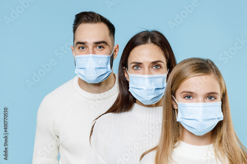 Young parents mom dad with child kid daughter teen girl in sweaters sterile face mask safe from coronavirus virus covid-19 during quarantine isolated on blue background. Family day parenthood concept.