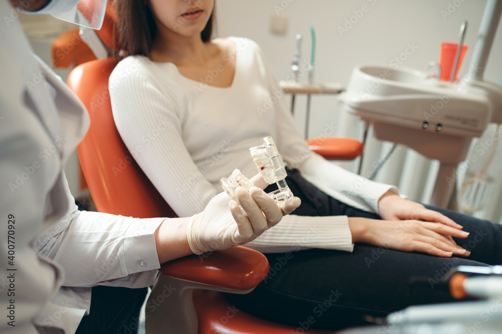 Caucasian brunette sits on a couch while the doctor shows her a jaw model Caucasian brunette sits on a couch while the doctor shows her a jaw model