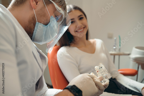 Doctor in a protective mask tells a smiling caucasian girl how to brush her teeth properly