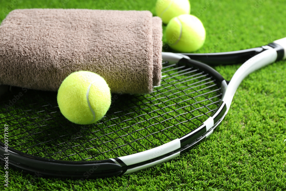 Tennis racket, towel and balls on green grass, closeup. Sports equipment