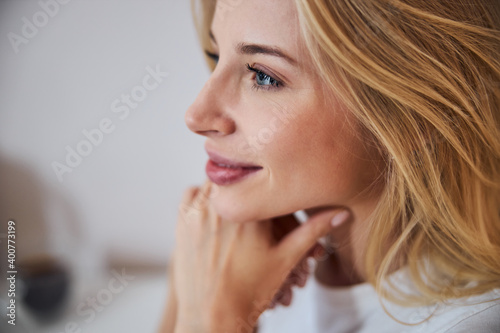 Charming attractive blonde female in white shirt looking away while enjoying great time in home