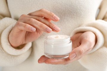 Woman holding jar of moisturizing cream, closeup. Cosmetic product for winter