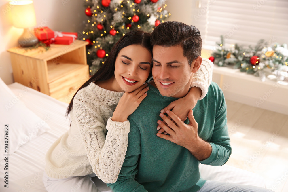 Happy couple on bed near Christmas tree at home Happy couple on bed near Christmas tree at home