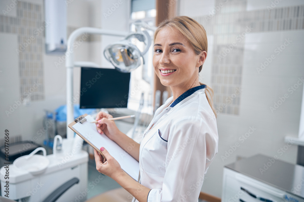 Smiling beautiful dentist making notes in office Smiling beautiful dentist making notes in office