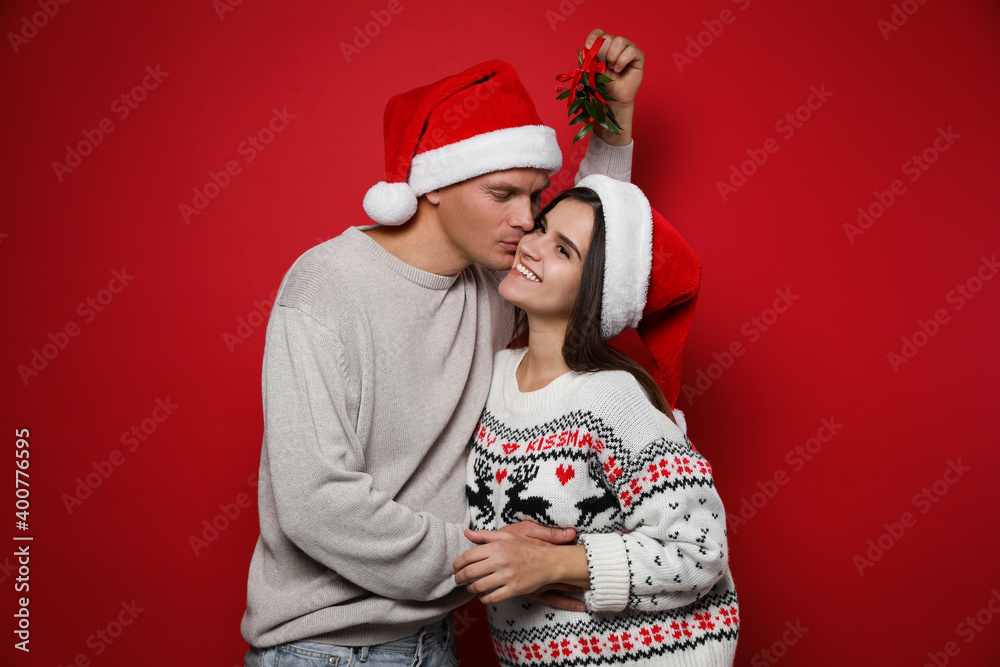 Fototapeta premium Happy couple under mistletoe bunch on red background