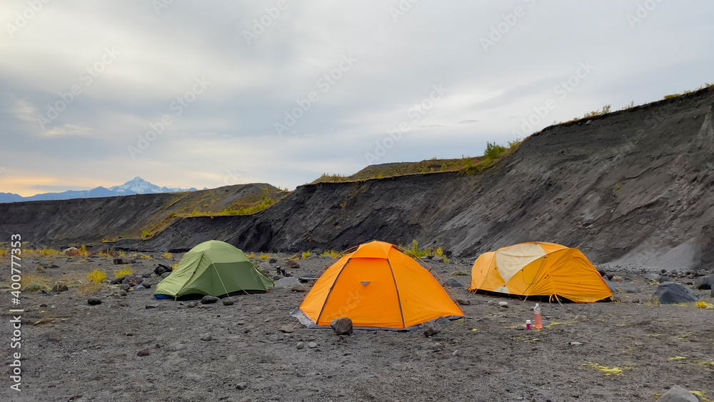 Expeditionary extreme tents of different colors stand in a small ravine on the lava fields of Kamchatka