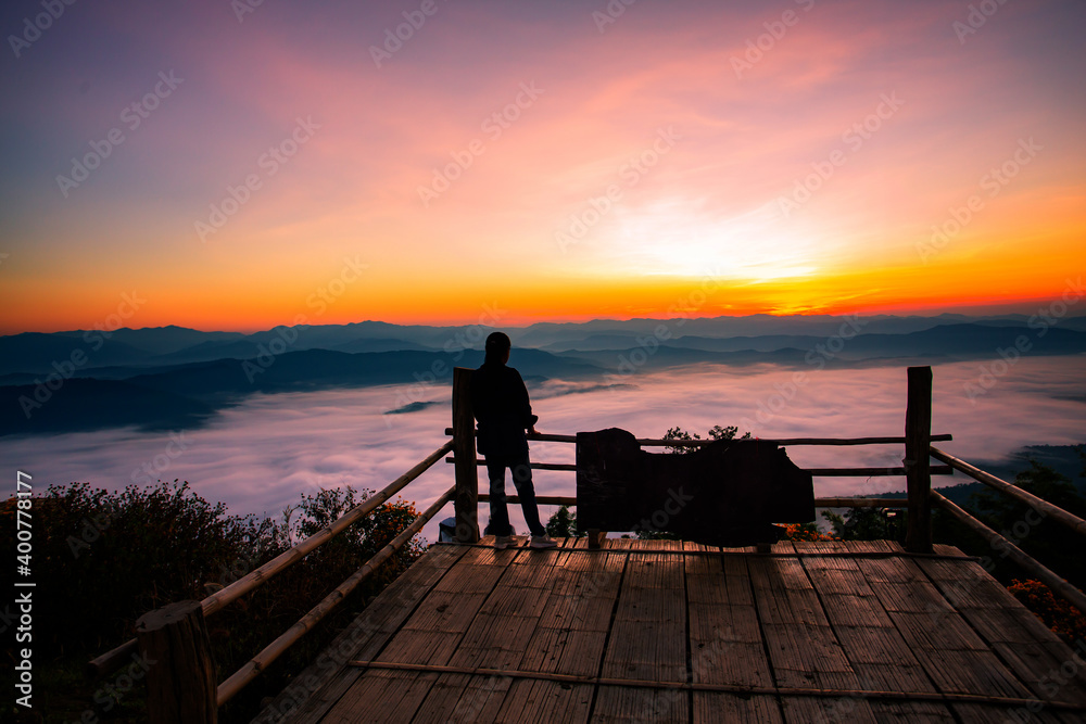 Fototapeta premium The silhouette of a woman sitting in front of the sunrise on the hill with the sea of ​​clouds In the north of Thailand, Doi Samer Dao, Nan Province