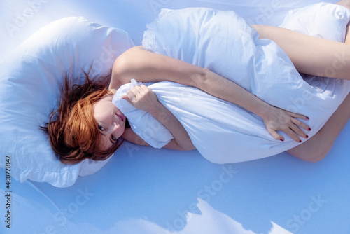 Fotografia View from above to an attractive, young, sexy, redhead, woman in sunlight cuddles in bed and hugs the soft comforter in the bedroom, copy space
