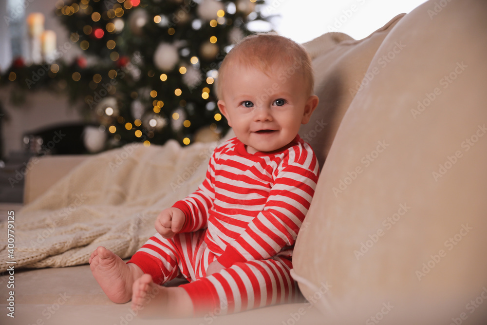 Cute baby in bright Christmas pajamas sitting on sofa at home Cute baby in bright Christmas pajamas sitting on sofa at home