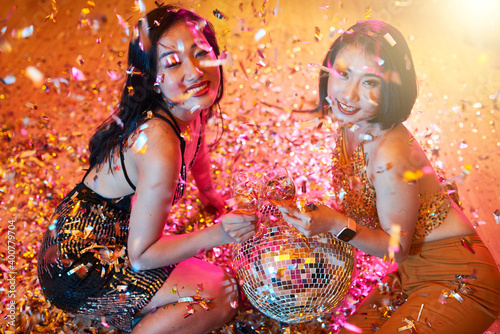 Pretty young Vietnamese women posing with disco ball and champagne glasses under falling confetti in night club