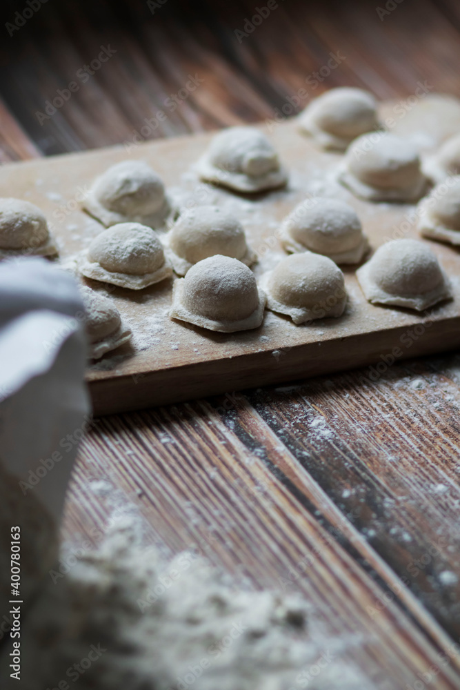 
Cooking dumplings. Raw dumplings lie on a wooden board. Nearby lies flour, rolling pin and dough against a background of wood.