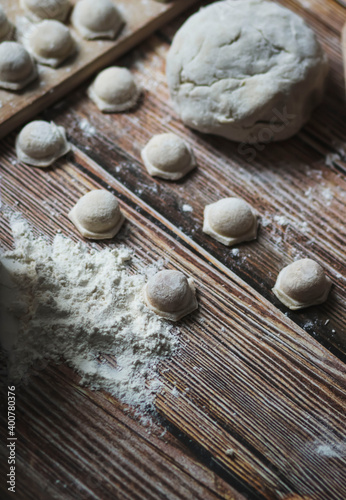  Cooking dumplings. Raw dumplings lie on a wooden board. Nearby lies flour, rolling pin and dough against a background of wood.