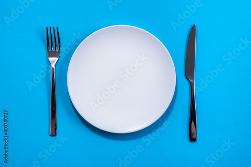 White plate with Utensils on blue background. Selective focus. Shot from above