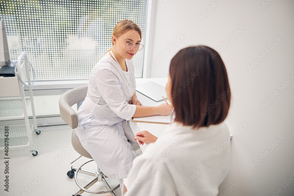 Attentive cosmetologist looking at her female client Attentive cosmetologist looking at her female client