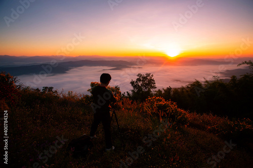 A photographer taking pictures of the sunrise And beautiful fog on the top of a tall mountain in Thailand
