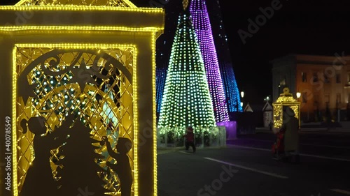 Evening Russia, Samara, Kuibyshev Square, New Year trees completely decorated with bulbs glow with different patterns and people walk. Christmas lantern in human growth new year decoration photo