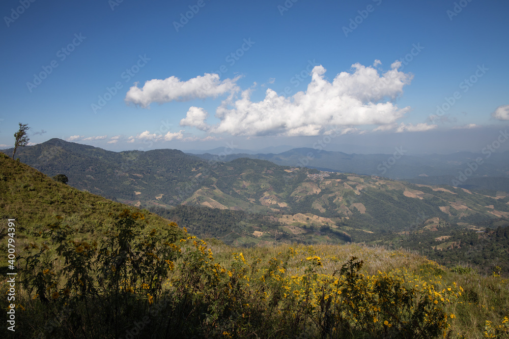 A mountain range with white clouds over the top showing the green valley and village in the north of Thailand. 
