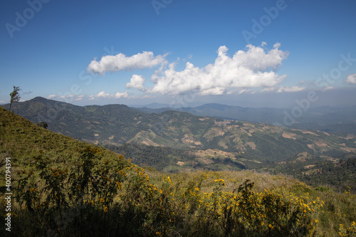 A mountain range with white clouds over the top showing the green valley and village in the north of Thailand. 