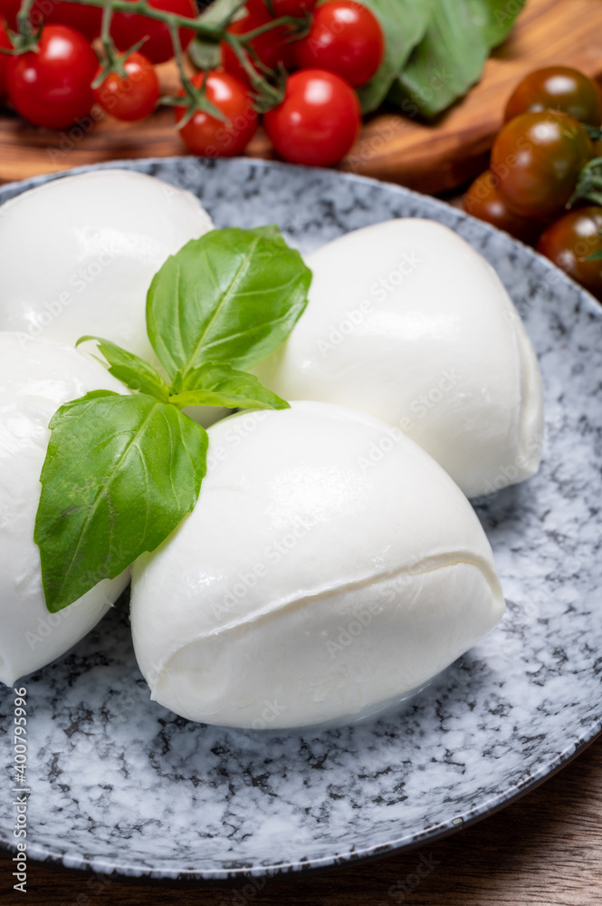 Cheese collection, white balls of soft Italian cheese mozzarella, served with red cherry tomatoes, fresh basil leaves