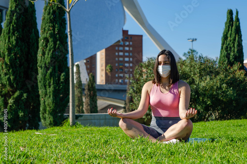 Young Brunette Woman with White Mask and Pink Tracksuit Meditating at the City Park in Summer