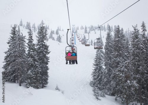 Ski lift carrying skiers over snow-covered fir trees on the mountainside. cold winter cloudy day. winter active rest © Anna