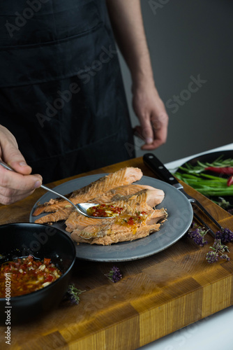 Chief cook is seasoning with chili sauce carved fish baked in salt crust. Seafood cooking. Salmon or seabass under salt crust with vegetables.