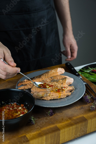 Chief cook is seasoning with chili sauce carved fish baked in salt crust. Seafood cooking. Salmon or seabass under salt crust with vegetables.