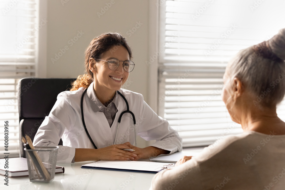 Smiling young female doctor talk consult mature patient at consultation in private clinic. Happy caring woman GP or therapist have meeting with senior client in hospital. Elderly healthcare concept. Smiling young female doctor talk consult mature patient at consultation in private clinic. Happy caring woman GP or therapist have meeting with senior client in hospital. Elderly healthcare concept.