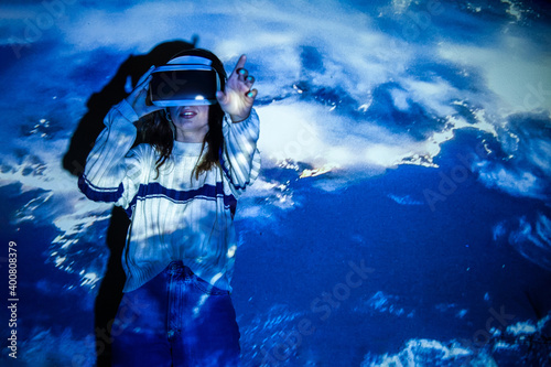 Woman using virtual reality headset, moving hand at interactive technology exhibition with multicolor projector light illumination, immersive concept photo