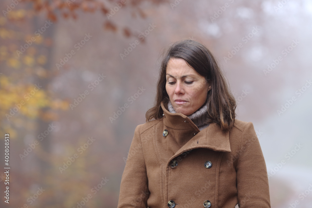 Sad woman walking alone in a park in winter Sad woman walking alone in a park in winter