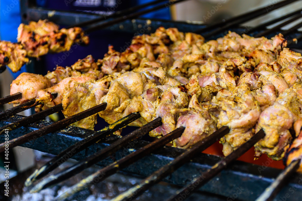 Closeup of skewed chicken legs tandoori slowly cooking over charcoal
