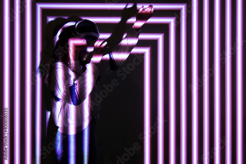 Woman using virtual reality headset, moving hand at interactive technology exhibition with multicolor projector light illumination, immersive concept