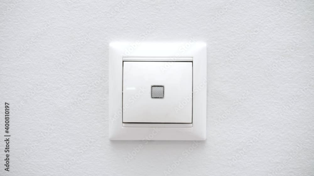 White switch on a light wall. Switch the button to turn on the light in the room. Turning on and off the lighting in the room. Close-up White switch on a light wall. Switch the button to turn on the light in the room. Turning on and off the lighting in the room. Close-up